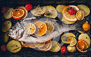 Sea gilt-head bream fish in the baking tray baked with potatoes, rosemary, lemon, orange, olives, tomatoes, onion and lime.