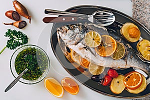 Sea gilt-head bream fish on the plate baked with potatoes, rosemary, lemon, orange, olives, tomatoes and lime.