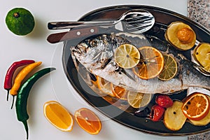 Sea gilt-head bream fish on the plate baked with potatoes, rosemary, lemon, orange, olives, tomatoes and lime.