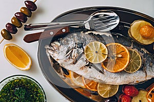 Sea gilt-head bream fish on the plate baked with potatoes, rosemary, lemon, orange, olives, tomatoes and lime.