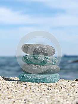 Sea glass on beach sand with seascape background. Beachcombing. Harmony and balance concept. Vertical composition