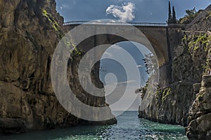 The sea glistens under the imposing arched bridge at Fiordo di Furore on the Amalfi Coast, Italy