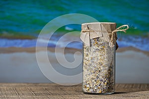 Sea himalayan salt with dry lavender and chamomile flowers in a glass jar on wooden table with the blue sea water background on a