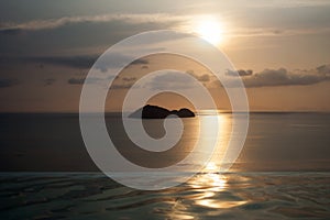 Sea island on the skyline behind infinity pool under beautiful sunset sky