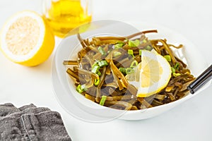 Sea kale kelp salad with oil and lemon in a white plate, white b