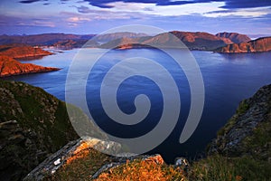 Sea landscape in the Norway. Evenig pink light on the ocean coast. Rocky cost in the summer night. Water surface with beautiful li