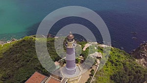 Sea lighthouse on mountain cliff and sailing ships drone view. Aerial landscape sea light house on green mountain and