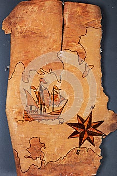 Sea map with illustrations of sailing vessel and compass rose on the order of antiquities on natural wooden background from birch photo