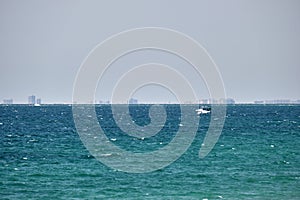 Sea panorama. Small motor boat floats in deap blue bay water under bright blue sky, tall buildings on distant shore