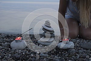 Sea pebble tower on the beach at sunset, with candles close up.