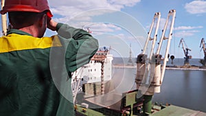 Sea port worker looking at wheat loading to bulker ship cargo container at sea grain elevator. Grain shipment from silos