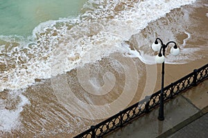 sea promenade with lantern and sand beach in stormy weather with waves