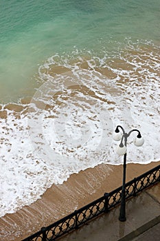 sea promenade with lantern and sand beach in stormy weather with waves