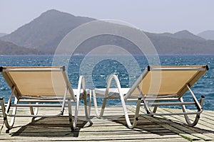 Sea resort, two empty deck chairs on a wooden pier on green mountains background