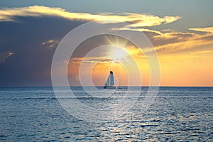 Sea and sailboat over cloudy sky and sun during sunset in Cozumel, Mexico