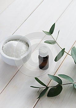 Sea salt, a bottle of essential oil and a branch of eucalyptus on a light wooden background