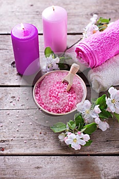 Sea salt in bowl, towels, candles and flowers on white wooden ba