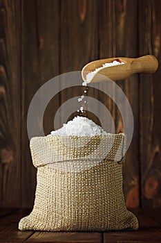 sea salt falling from scoop in sack on wooden table