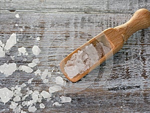 Sea salt flakes and wooden spoon over bark on wooden background