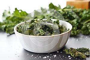 sea salt sprinkled kale chips in a dish on light background