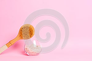 Sea salt and a wooden brush for dry massage on a pink background