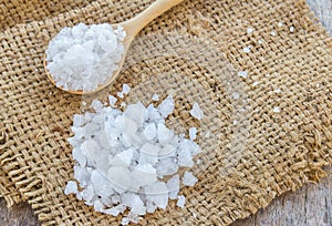 Sea salt in wooden spoon on burlap sack background