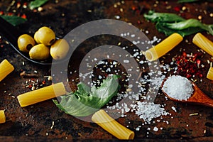 Sea salt in wooden spoon surronded by pasta and other ingredients.