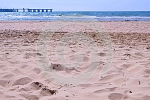 Sea sand beach with stormy waves and pier view at sunny windy day.