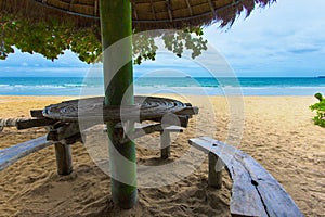 Sea sand and sun looking from beautiful and peaceful beach under big green tree. The beach has sitting area bench and little cocon