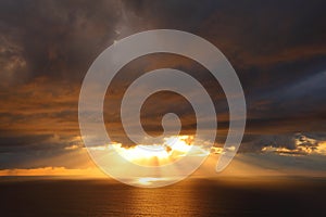 Sunbeams through storm clouds over ocean by golden sunrise photo