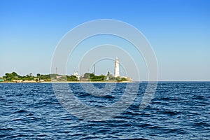 sea shore with buildings and a white lighthouse on a sunny summer day