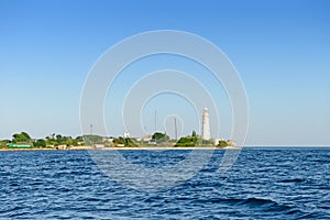 sea shore with buildings and a white lighthouse on a sunny summer day