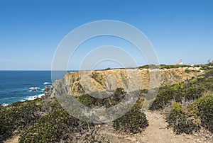 Sea shore and cliff with red and white historic Portugese lighthouse Cabo Sardao building on Ponta do Cavaleiro, Rota