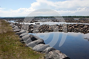 Sea stone dam and serpantine embankments on the background of the arched dam gates