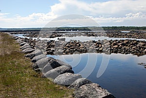 Sea stone dam and serpantine embankments on the background of the arched dam gates photo