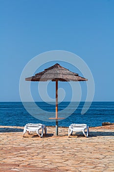 Sea with sun umbrella, white deckchair on flagged stone beach. Vactaion, travel background, Croatia, Istria