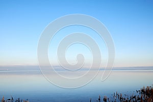 Sea at sunset with clear blue sky making a nature mirror reflection on the water with golden grey clouds on the horizon