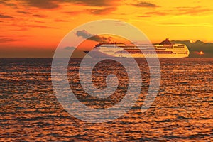 Sea at sunset with light ripples on the water and dramatic clouds, a large cruise liner on the horizon