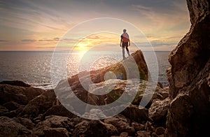 Sea sunset view. Man with backpack on the rocks