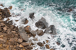 Sea surf, turquoise ocean waves beat against rocky shore. High tide time, water foams and splashes