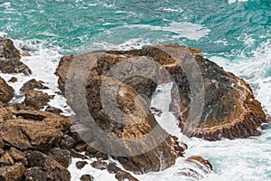 Sea surf, turquoise ocean waves beat against rocky shore. High tide time, water foams and splashes