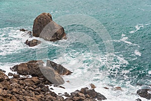 Sea surf, turquoise ocean waves beat against rocky shore. High tide time, water foams and splashes