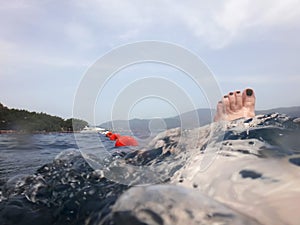 Sea surface with buoys, woman legs under water and mountains in the distance. View and shooting from water