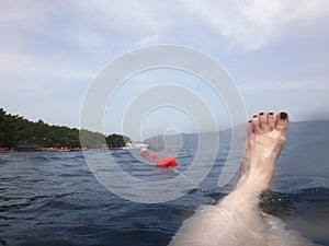 Sea surface with buoys, woman legs under water and mountains in the distance. View and shooting from water