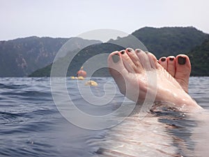 Sea surface with buoys, woman legs under water and mountains in the distance. View and shooting from water