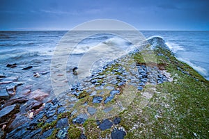 Sea surrounded by rocks covered in mosses under the cloudy sky in the evening