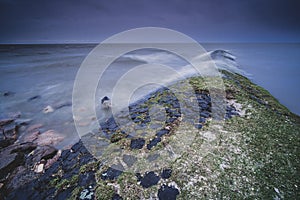 Sea surrounded by rocks covered in mosses under the cloudy sky in the evening