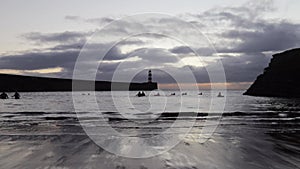 Sea swimmers swimming in a harbour at sunrise with lighthouse in the background