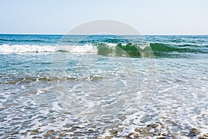 Sea tidal waves with white foam on a sunny sandy beach in resort