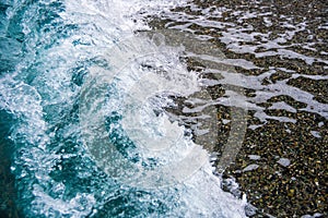 Sea tide on a pebble shore. Waves with white foam on a pebble beach. Nature concept, background